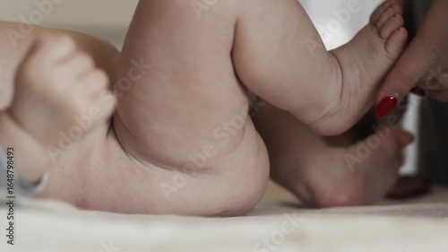Newborn baby with naked booty is lying on table waiting for enema procedure at home, clyster. Constipation Diarrhea concept. Meteorism tympany, disease. Mom holds baby legs. Infant parental care