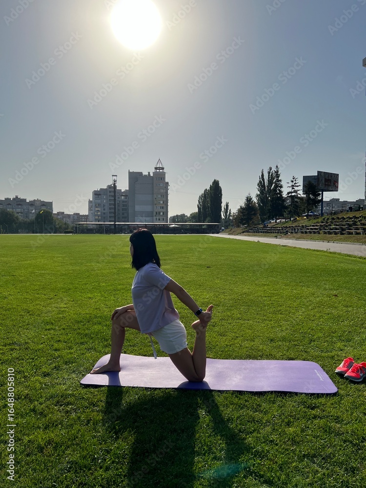 Fototapeta premium Woman Stretching on Yoga Mat Outdoors in Morning Sunlight
