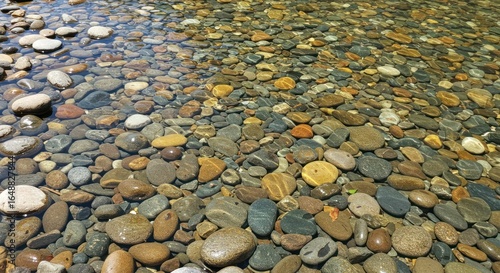 Shallow water flowing over riverbed with many smooth round rocks and pebbles.