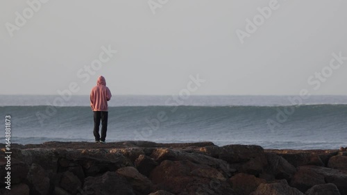 4K 50fps footage of a man standing on a stone jetty observing surfers riding incredible waves. Filmed on a cold morning with perfect conditions for surfing. Atlantic Ocean, Portugal.
