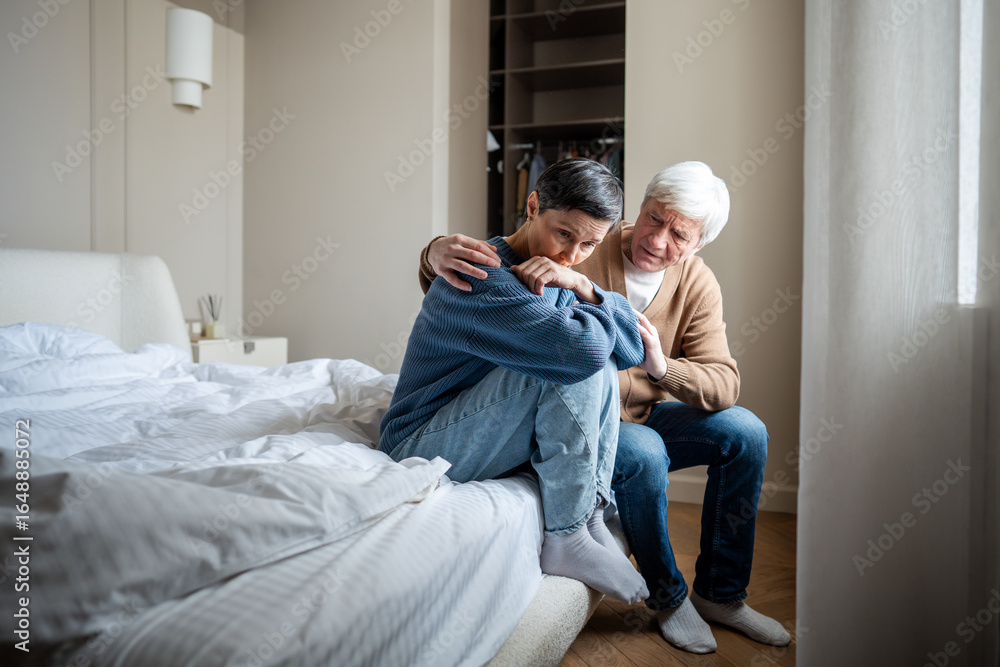 Fototapeta premium Elderly couple in grief. Mature wife in distress wronged in sorrow, marital disagreement, husband calming embrace and giving water. Conflict resolution, emotional repair, stress relief, reconciliation