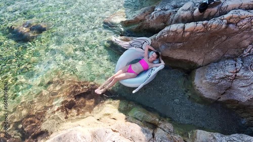 view from above of woman on inflatable swan in shallow turquoise bay between rocks in Kostrena, Croatia