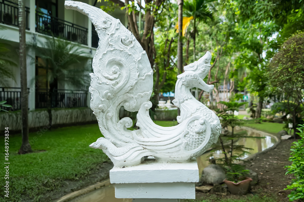 Obraz premium Ornate white stone sculpture of mythical bird with foliage backdrop in a lush garden setting
