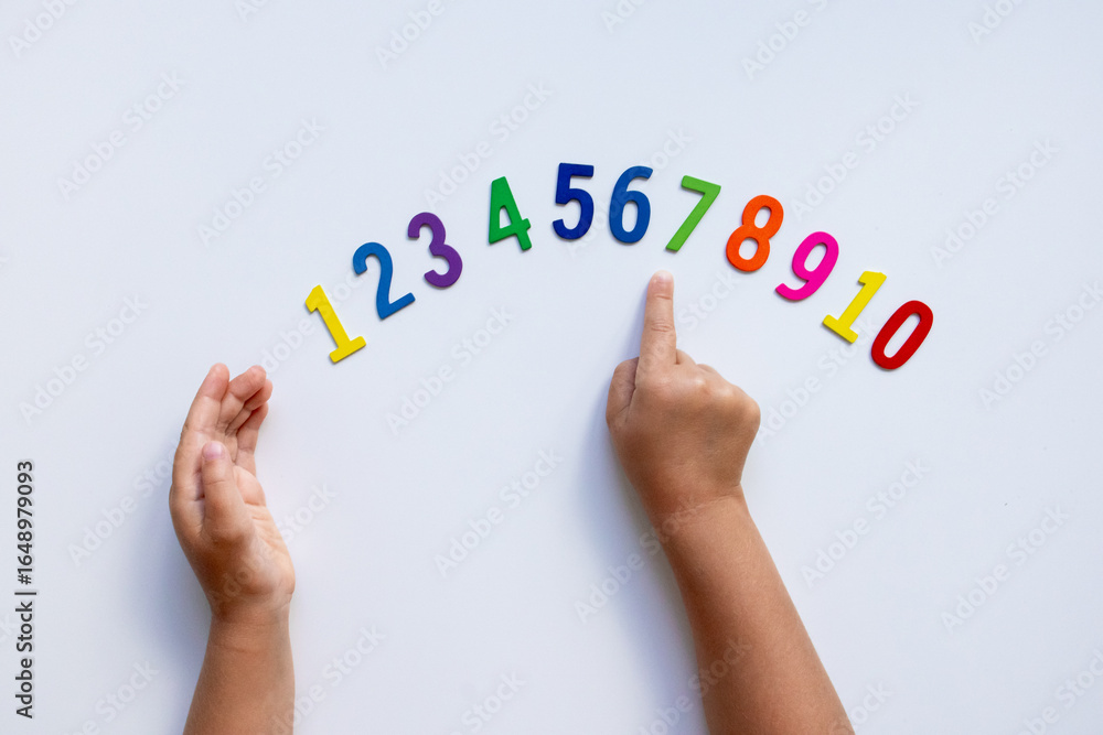 Fototapeta premium Child hands pointing at colorful wooden numbers on white background