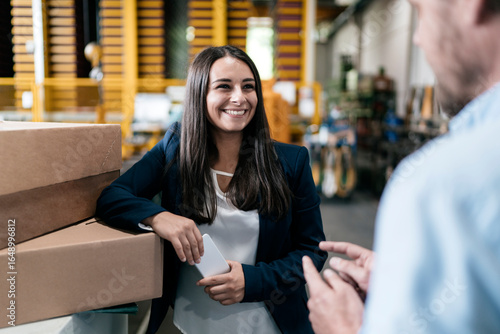 Young woman working in distribution warehouse, talking to colleague