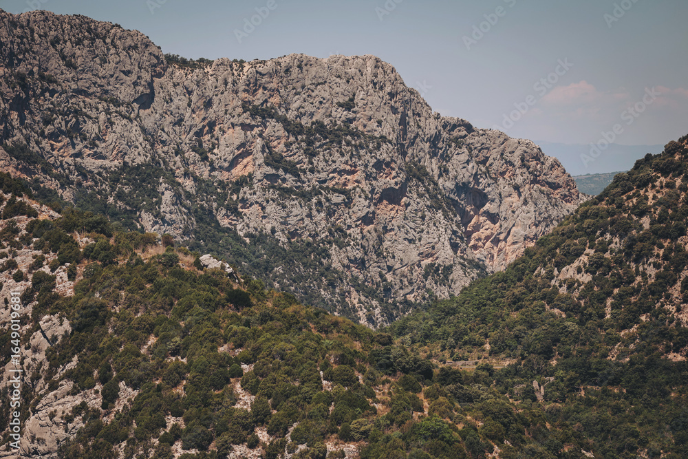Obraz premium Majestic rock formations rise above lush valleys under a clear sky in a tranquil mountain landscape at midday