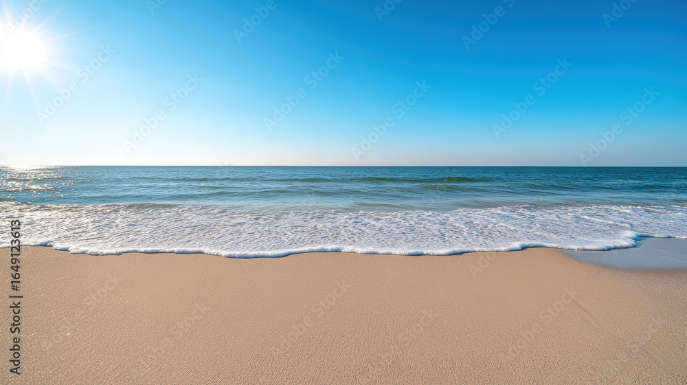 Fototapeta premium Bright beach scene with gentle waves lapping at shore under clear blue sky