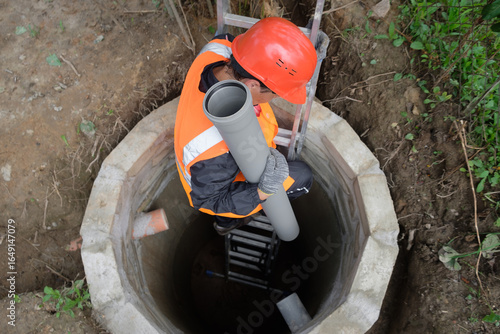 Worker in protective gear installing and inspecting septic system pipes inside a manhole at a private house, ensuring proper drainage, maintenance, and local wastewater management	