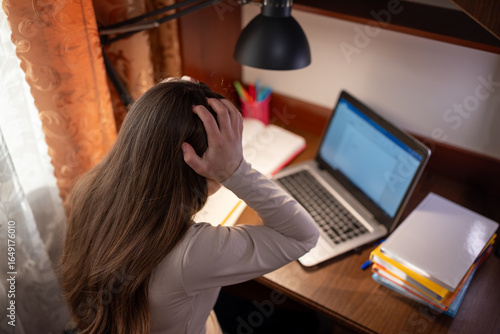 Student in despair over an incomprehensible task on her laptop. A girl sits at a desk with a laptop, holding her head, she doesn't understand the task and is in despair