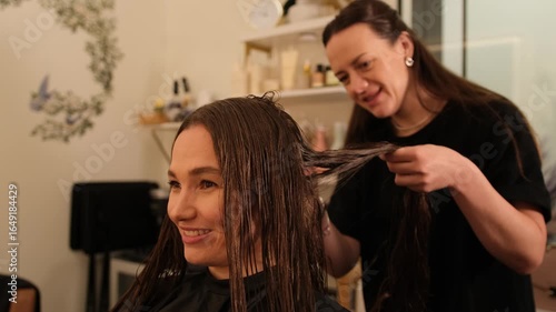 Smiling hair stylist working on female client in bright salon