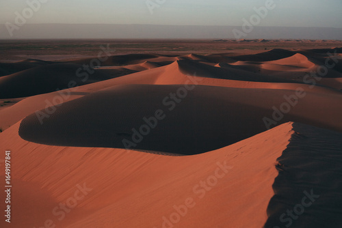 Edge of the Sahara near Lion Dune, Morocco – few sand dunes with footprints in foreground, fading into endless flat desert expanse at sunset, serene desert landscape