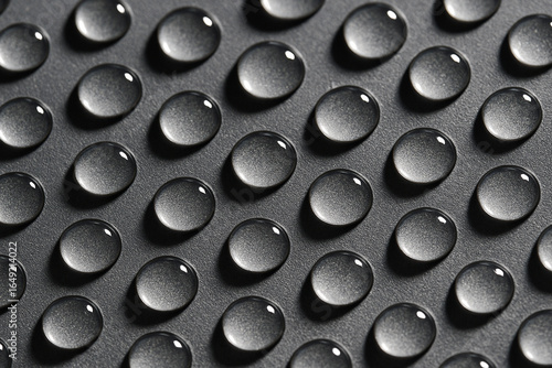 Detailed macro shot of repetitive uniform water droplets aligned in neat rows on a grey metallic surface