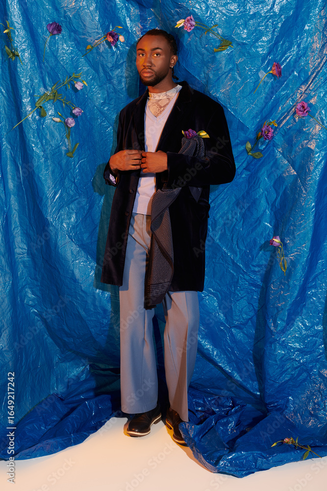 Fototapeta premium Handsome young man poses elegantly against a vibrant blue backdrop adorned with flowers