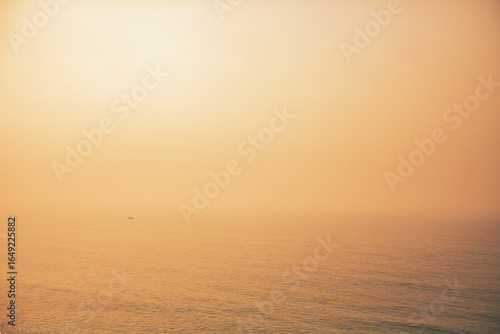 Mystical golden sunset over the sea in Portugal, fog blending horizon and sky, artistic and atmospheric coastal seascape, serene and dreamy landscape