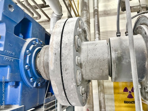 High-pressure industrial pump coupling in a specialized manufacturing facility, featuring heavy-duty bolted flanges and a clear 