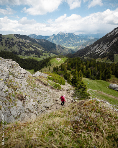 Hiker in Red Jacket Descending Rocky Mountain Slope with Scenic Valley View