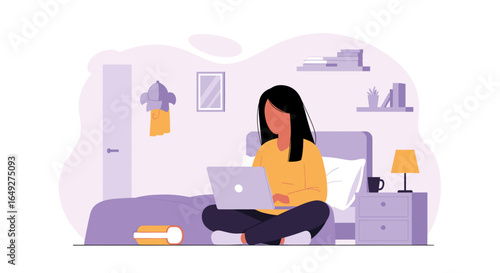 Young woman comfortably working on her laptop computer while sitting cross-legged on her bed.