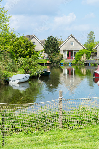 Typical beautiful Dutch landscape with some houses near the canal and a boat on the water. Typical summer day in the Dutch suburb with green trees and living area