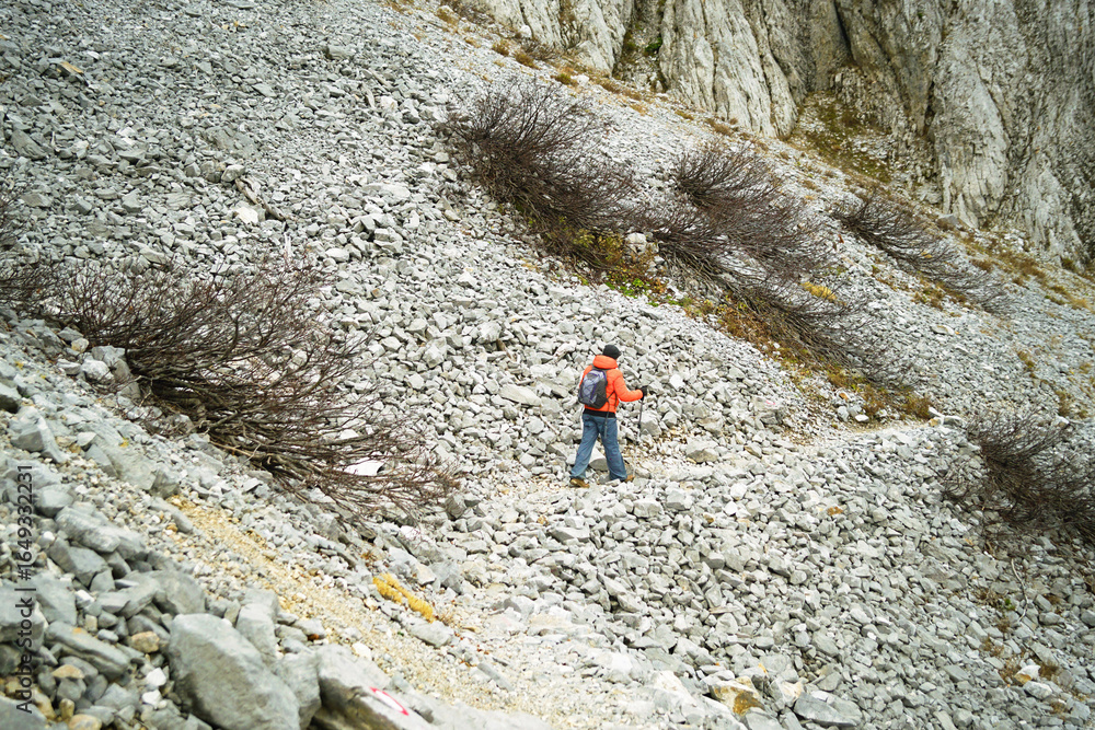 Tourist crosses steep scree slope. Concepts of hiking challenge, outdoor lifestyle, eco-conscious travel and discovering Montenegro mountain landscapes. Exploring the circular route around Komovi Tourist crosses steep scree slope. Concepts of hiking challenge, outdoor lifestyle, eco-conscious travel and discovering Montenegro mountain landscapes. Exploring the circular route around Komovi