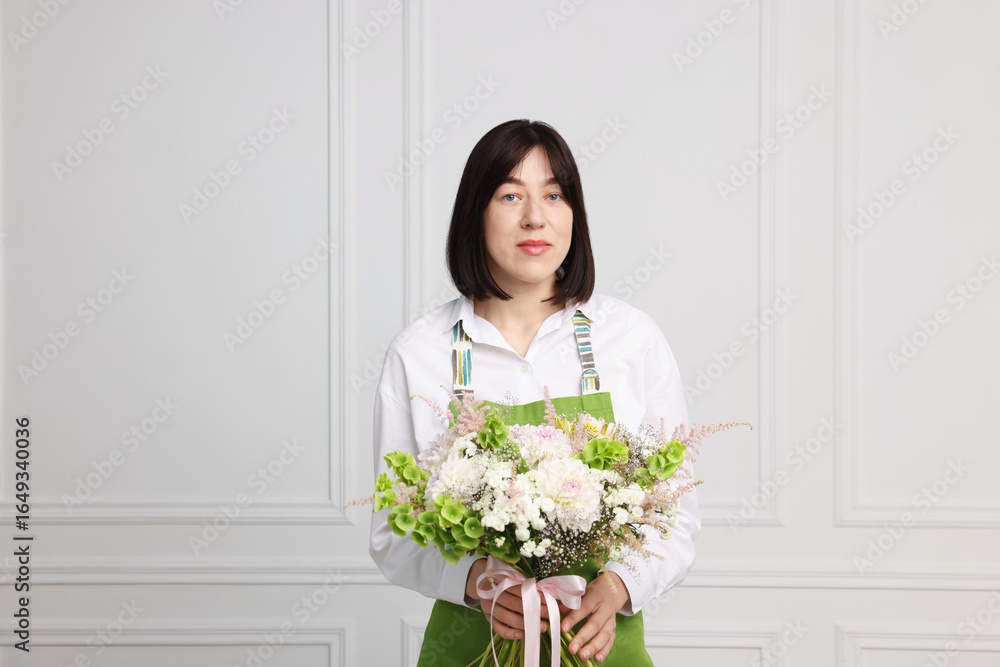 Florist with beautiful bouquet of flowers near white wall indoors Florist with beautiful bouquet of flowers near white wall indoors