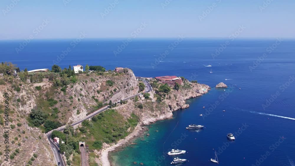 A stunning aerial view of Taormina, Sicily, captured by a drone, shows a picturesque bay dotted with luxury yachts against the stunning Mediterranean coastline. A stunning aerial view of Taormina, Sicily, captured by a drone, shows a picturesque bay dotted with luxury yachts against the stunning Mediterranean coastline.