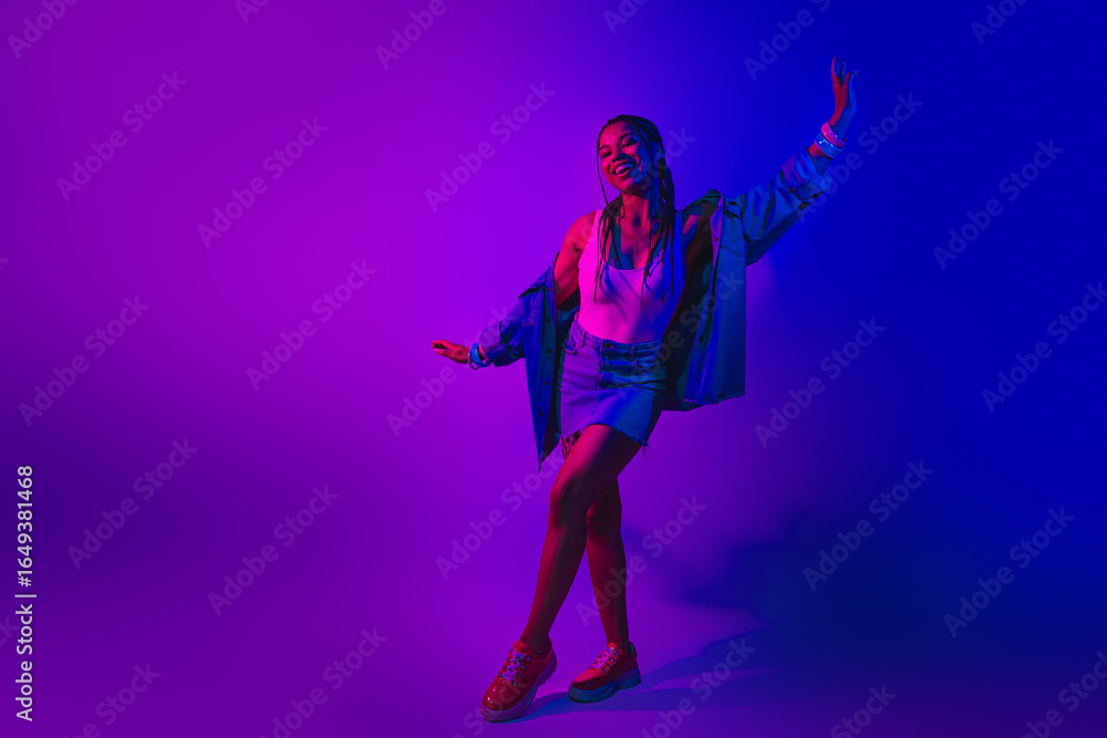 Fototapeta premium Lovely woman dancing in vibrant neon lights, wearing denim jacket and skirt, embracing the fun of disco nightlife