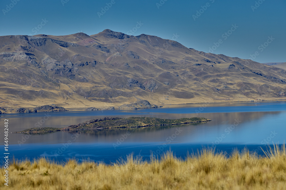 Fototapeta premium Deep blue waters embrace golden highland hills at Lagunillas Lake near Puno — a serene Andean sanctuary of beauty and calm
