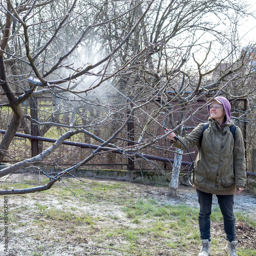 A woman works in the spring garden and spray with a rechargeable sprayer chemicals against pests