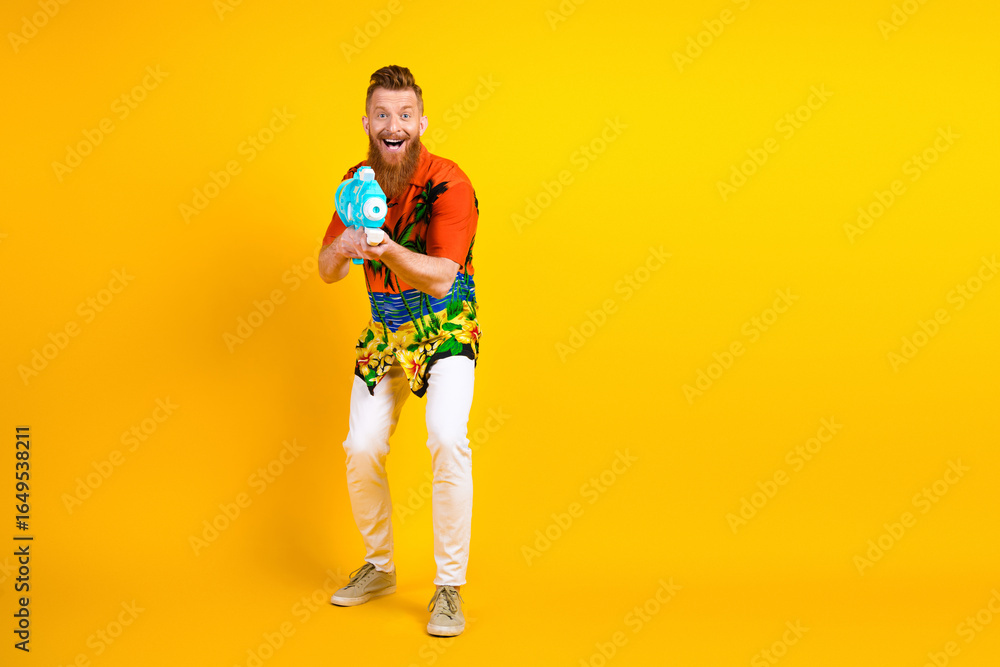 Fototapeta premium Cheerful man in tropical shirt having fun with water toy against vibrant yellow background