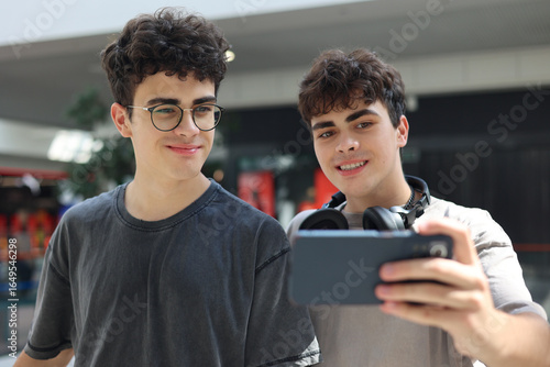 Foto Two cheerful teenage twin brothers standing together and smiling while looking at a smartphone during a video call or live stream indoors
