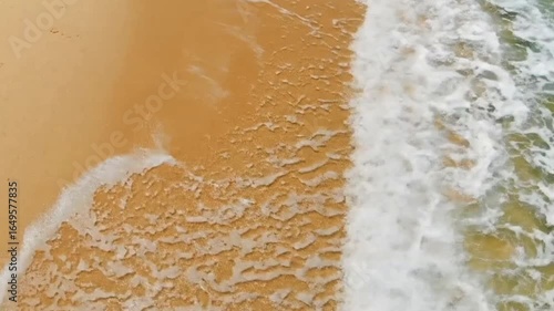 A beach scene with waves washing over the sand creating a textured foamy surface
