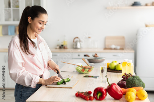 Canvas Print Portrait of happy young woman cooking delicious and healthy food standing in modern kitchen at home