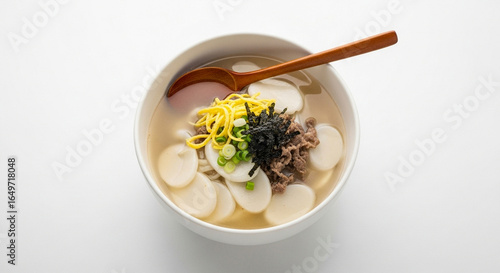 A traditional Korean rice cake soup, Tteokguk, in a white bowl with beef, egg, and seaweed garnish.