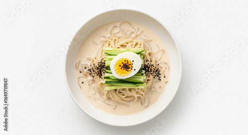 A bowl of Korean cold soy milk noodle soup, Kong-guksu, garnished with fresh cucumber, a halved boiled egg, and black sesame seeds, viewed from above.