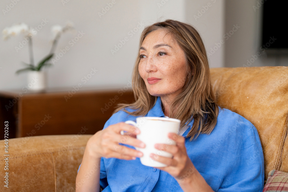 Woman enjoying a warm drink while relaxing in a cozy living room filled with natural light during a peaceful afternoon Woman enjoying a warm drink while relaxing in a cozy living room filled with natural light during a peaceful afternoon