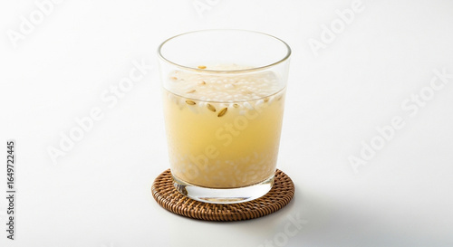 A glass of traditional Korean sweet rice punch, sikhye, with floating rice grains on a woven coaster against a white background.
