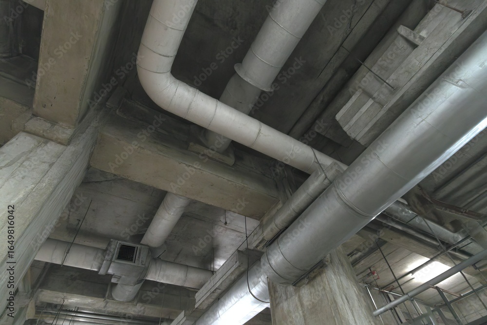 Obraz premium Industrial infrastructure pipes and ducts beneath a concrete structure.