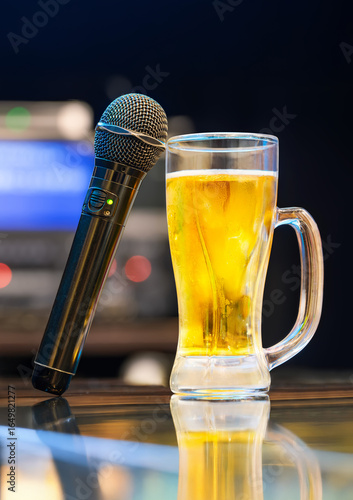 A close-up of a black karaoke microphone with green light and a glass of golden japanese beer on a glossy bar counter, evoking a lively and relaxed mood in a modern entertainment setting.