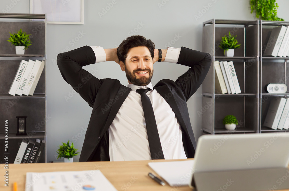 Naklejka premium Break from office work for happy businessman sitting at desk with satisfied expression on face. Man sitting in boss pose, leaning back in chair, hands behind head. Relax in comfort, easy life concept