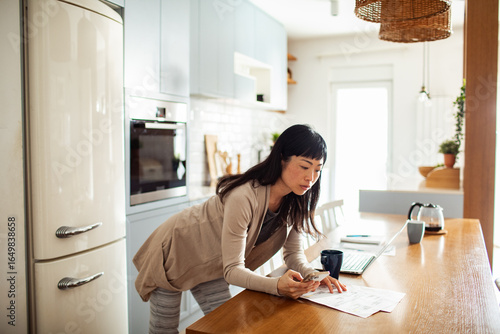Woman reviewing utility bill at home while using laptop in bright kitchen