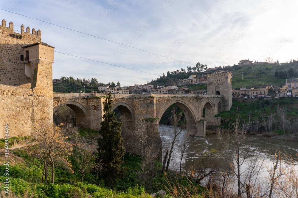 Toledo Bridge: Spain's historic San Martín Bridge, gracefully spanning the Tagus River, is steeped in history and culture, with medieval stone arches, towers, and a timeless design under a sunny sky Toledo Bridge: Spain's historic San Martín Bridge, gracefully spanning the Tagus River, is steeped in history and culture, with medieval stone arches, towers, and a timeless design under a sunny sky