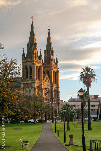 St Peters Cathedral glowing in warm sunrise light, viewed from parkland path in Adelaide, South Australia