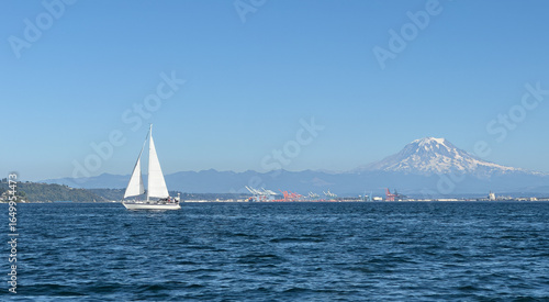 Isolated sailboat sailing in Puget Sound's Commencement Bay with the port of Tacoma and Mount Rainier in the distance. 