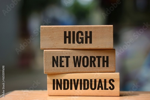 Wooden block with the words 'high, net worth, individuals' on an blurred background. The concept of wealth and finance.