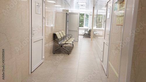 Empty corridor of a hospital or clinic with waiting chairs and examination rooms, healthcare and medical concept