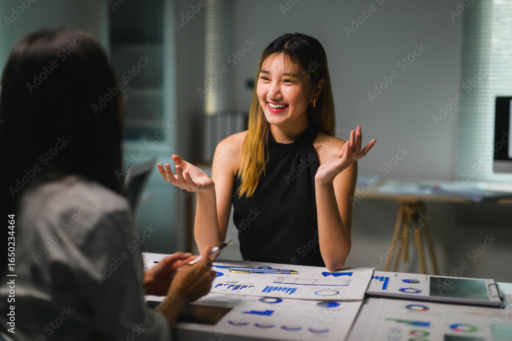 Fototapeta premium Asian businesswomen discussing and working late together using charts and graphs