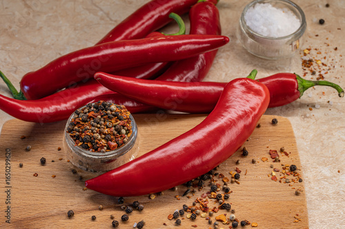 The pods of red chilli pepper, glass cup of peppercorn,  bowl of salt on wooden cutting board. Close up.