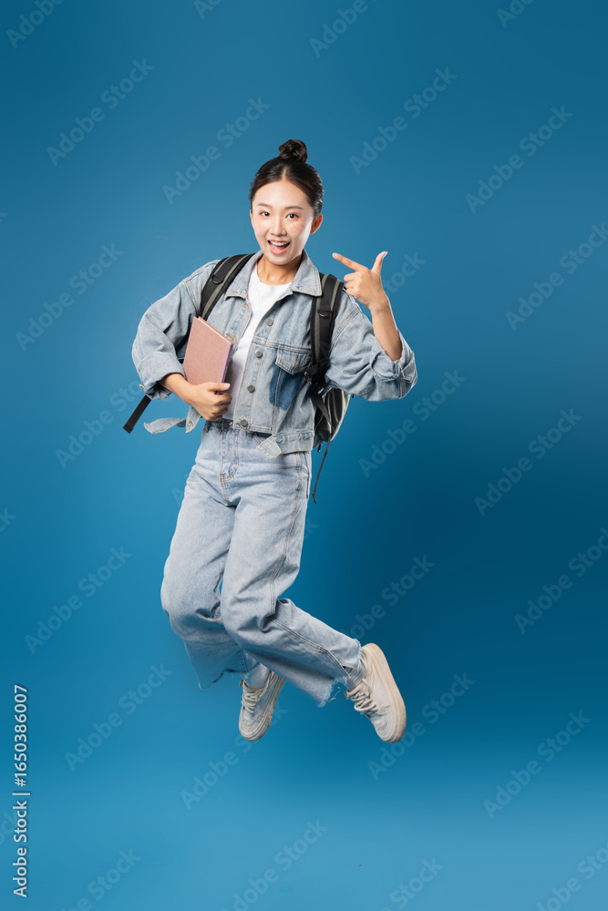 Obraz premium Energetic student leaps holding a book in a joyful pose against a vibrant blue backdrop