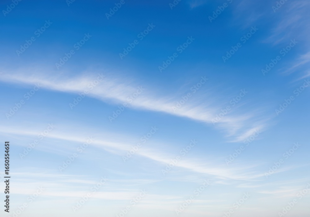 Obraz premium Wispy white clouds drift across a vast, clear blue sky on a bright, serene day, evoking a sense of peace and openness