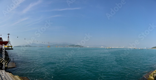 Panoramic view of a serene coastal scene with a pier, calm waters, and distant islands under a clear sky.